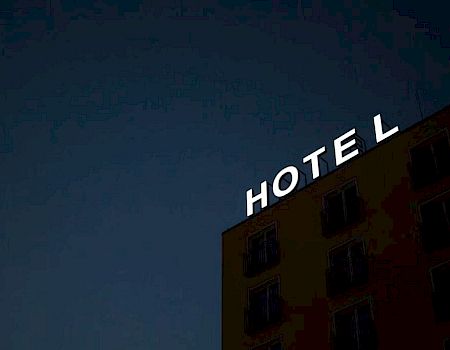 The image shows a building at night with an illuminated sign that reads "HOTEL," but the "L" is partially unlit, creating a unique visual.