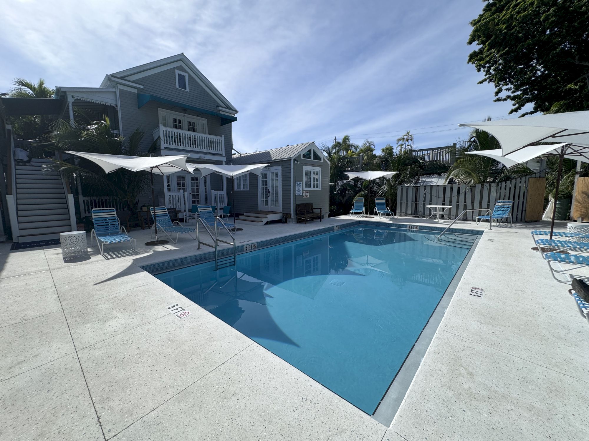 A modern house with a swimming pool, surrounded by lounge chairs and umbrellas on a sunny day, with blue skies above.