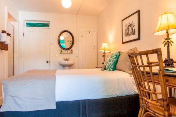 A cozy bedroom with a bed, a chair, a small sink, wall art, and lamps on a wooden desk.