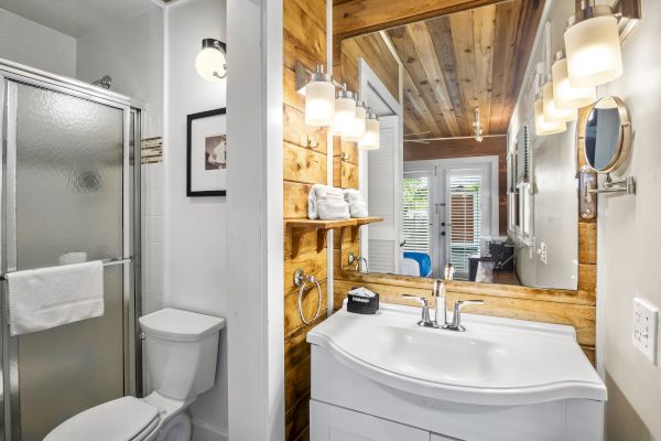 A modern bathroom features a shower, toilet, vanity with a sink, and wooden accents, illuminated by stylish light fixtures.