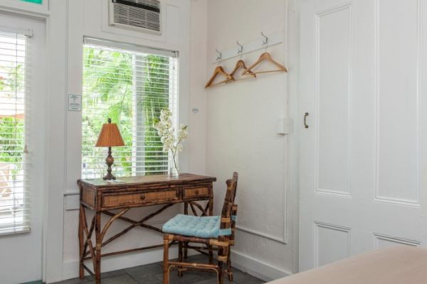 A simple room corner with a wooden desk, chair, lamp, and hangers on the wall, near a window with blinds.