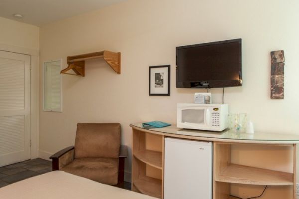 The image shows a room with a TV, microwave, mini fridge, chair, and shelves. A wall-mounted shelf for hanging clothes is also visible.