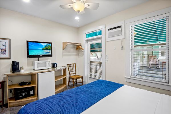 A cozy room with a bed, TV, microwave, and coffee maker. It has a window, chair, ceiling fan, and open closet space.