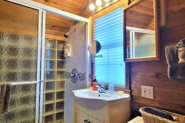 A cozy bathroom with a wooden interior features a shower, sink with mirror, and a shelf holding towels and a basket.