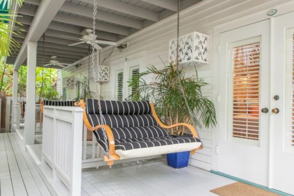 A porch with a black-striped swing, ceiling fan, potted plants, and white doors with blinds. Cozy and inviting atmosphere.