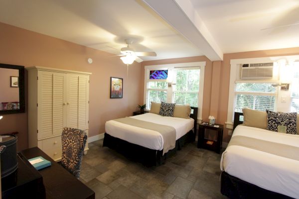 A cozy bedroom with two beds, a wardrobe, a desk, a chair, and a wall-mounted TV; air conditioning is visible by the window.