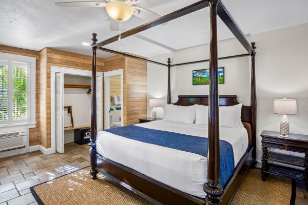 The image shows a bedroom with a four-poster bed, blue accent, nightstands, a lamp, open closet, tiled floor, and a ceiling fan.