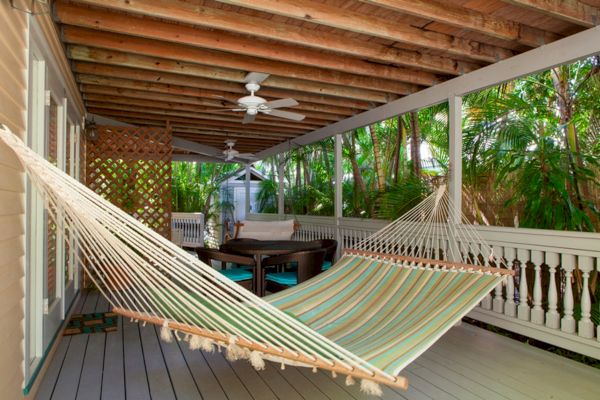 A cozy porch with a striped hammock, seating area, ceiling fans, and tropical plants, offering a relaxing outdoor space.