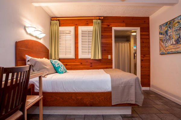 A cozy bedroom with wood paneling, a neatly made bed, a chair, and a painting on the wall.