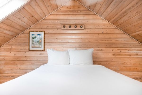 A cozy attic room with wooden walls, a neatly made bed, and a small framed picture on the left wall, creating a warm, inviting space.