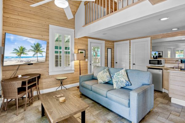 A cozy living room with a light blue sofa, wall-mounted TV, and small kitchenette. A wooden interior gives a warm, inviting feel.