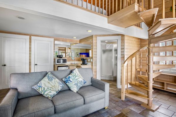 A cozy room featuring a spiral staircase, a gray sofa with patterned pillows, and a compact kitchen area in a modern, wooden interior design.