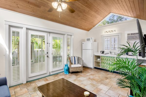 Cozy room with French doors, tiled floor, wooden ceiling, kitchenette, and a plant for decor. Natural light streams in beautifully.