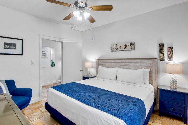 A cozy bedroom with a bed, blue accents, ceiling fan, and artwork on the walls, creating a relaxing and inviting atmosphere.