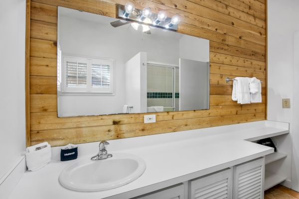 A bathroom with a white countertop, a sink, a large mirror, wood paneling, and a towel rack with white towels.