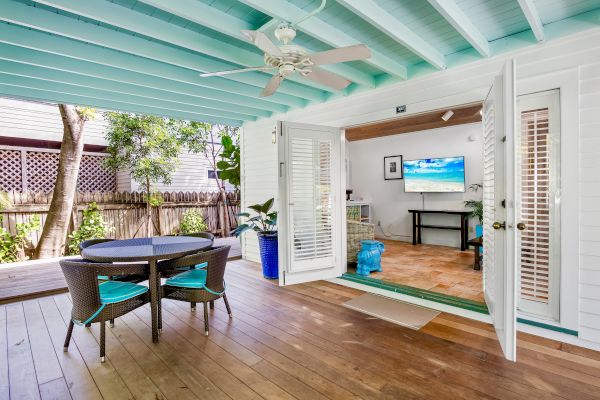 A cozy patio with a round table and chairs, leading into a living room with open doors and a TV on the wall.