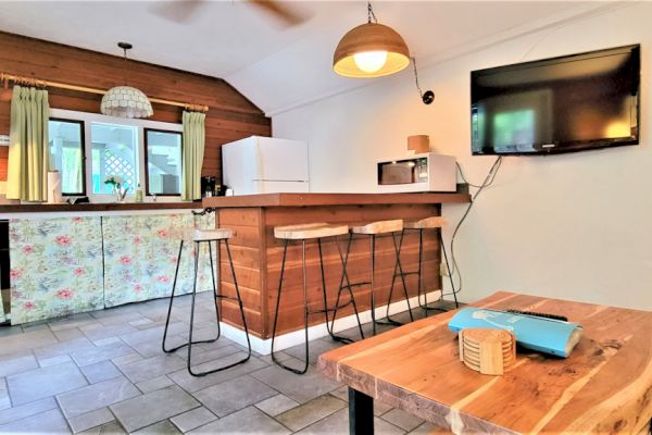 A cozy kitchen with wooden accents, a bar counter with stools, fridge, microwave, and a wall-mounted TV.