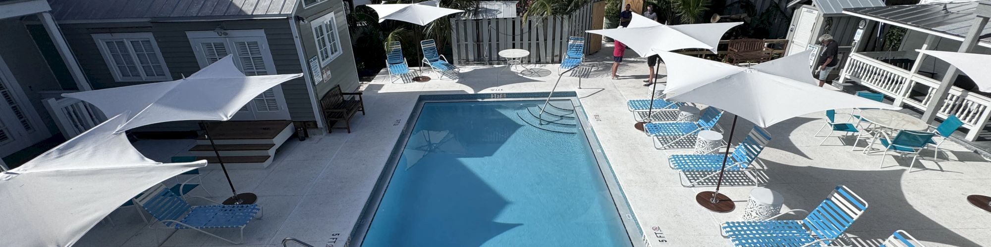 A swimming pool surrounded by blue lounge chairs and white umbrellas in a sunny outdoor setting.