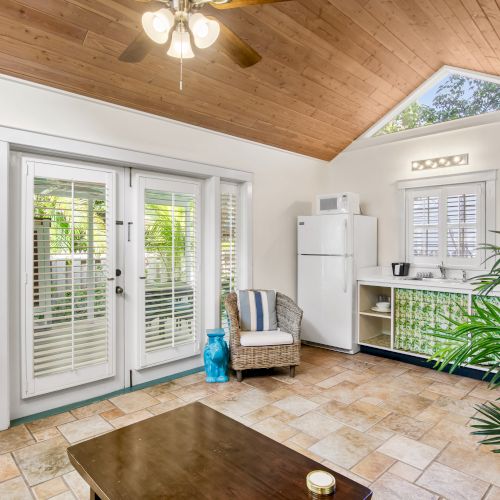 A cozy living space with a sloped wooden ceiling, tiled floor, large glass doors, and a small kitchenette.