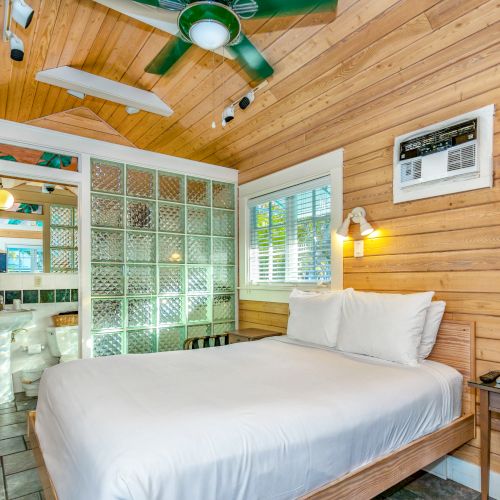 A cozy wooden bedroom with a ceiling fan, a bed, glass block walls, and a view into a bathroom.