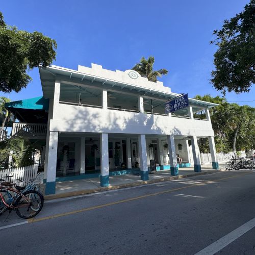 A two-story white building with blue trim, surrounded by trees and parked bicycles, under a clear blue sky.