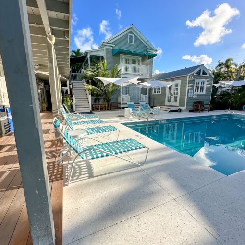 A poolside scene with lounge chairs, surrounded by a stylish house and clear blue sky, suggesting a relaxing atmosphere.